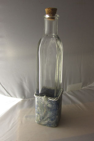 A glass bottle embellished with shimmery blue and translucent clays mixed together in a mokume-gane imitation style.