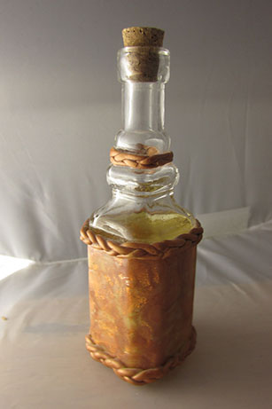 A glass bottle embellished with shimmery golden and translucent clays mixed together in a mokume-gane imitation style.
